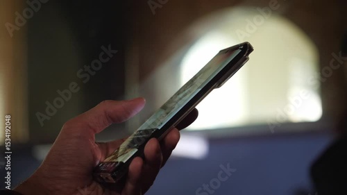A focused and modern mood is captured as a hand holds a glowing smartphone, its screen reflecting light, against a softly blurred background. This shot is ideal for illustrating digital connectivity