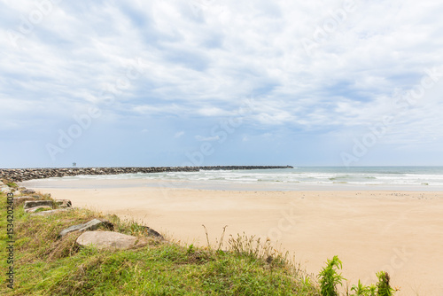 Rock wall curving around beach with sand and water and cloudy skies