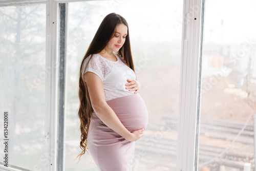 Free Download Pregnant woman in dress with very long hair on white background. Dreamy tender girl expecting a child. Portrait of beautiful pregnant woman in white shirt, smile. Window - GFXLoad