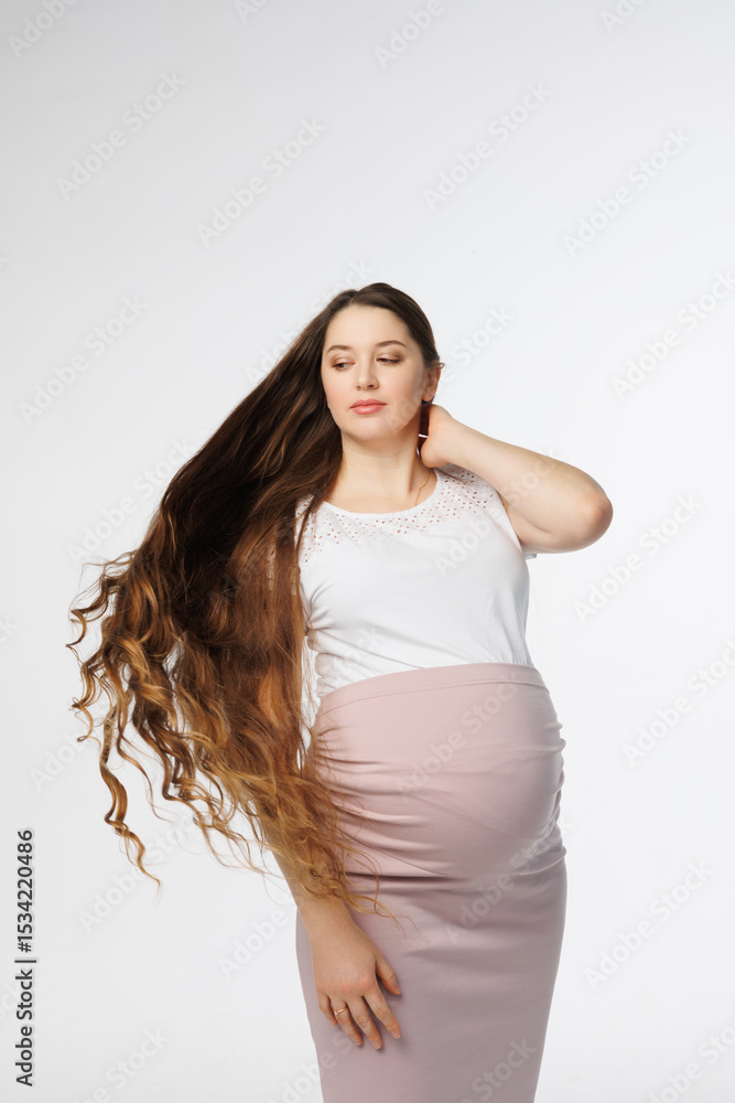 Pregnant woman in dress with very long hair on white background. Dreamy tender girl expecting a child. Portrait of beautiful pregnant woman in white shirt, smile. Window Pregnant woman in dress with very long hair on white background. Dreamy tender girl expecting a child. Portrait of beautiful pregnant woman in white shirt, smile. Window