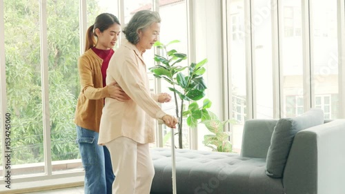 Female nurse who is taking care elderly woman with osteoarthritis needs cane help her walk to help her stand up and walk carefully and take care of her by being concerned and caring walk slowly.
