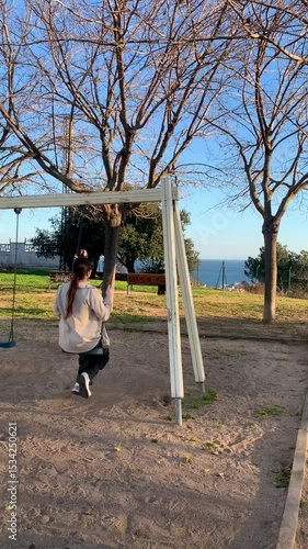Young woman swinging on a hillside swing at sunset with sea view, slow motion