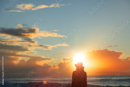 Silhouette eines jungen Mannes mit Hut bei Sonnenaufgang am Strand