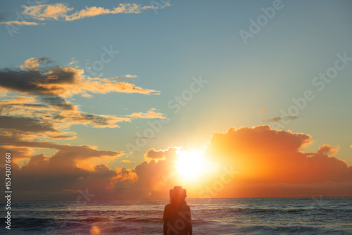 Silhouette eines jungen Mannes mit Hut bei Sonnenaufgang am Strand