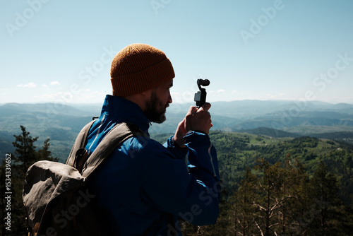 Man filming scenic mountain view with a compact gimbal camera on a sunny spring day in Zlatibor, Serbia. Travel blogger making video outdoor