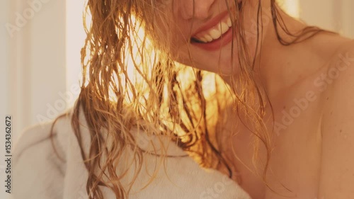 Beautiful cheerful woman wiping wet blonde hair drying with towel, looking at reflection in mirror bathroom long curls care. Happy girl close-up smilig face head. natural warm sun light white room