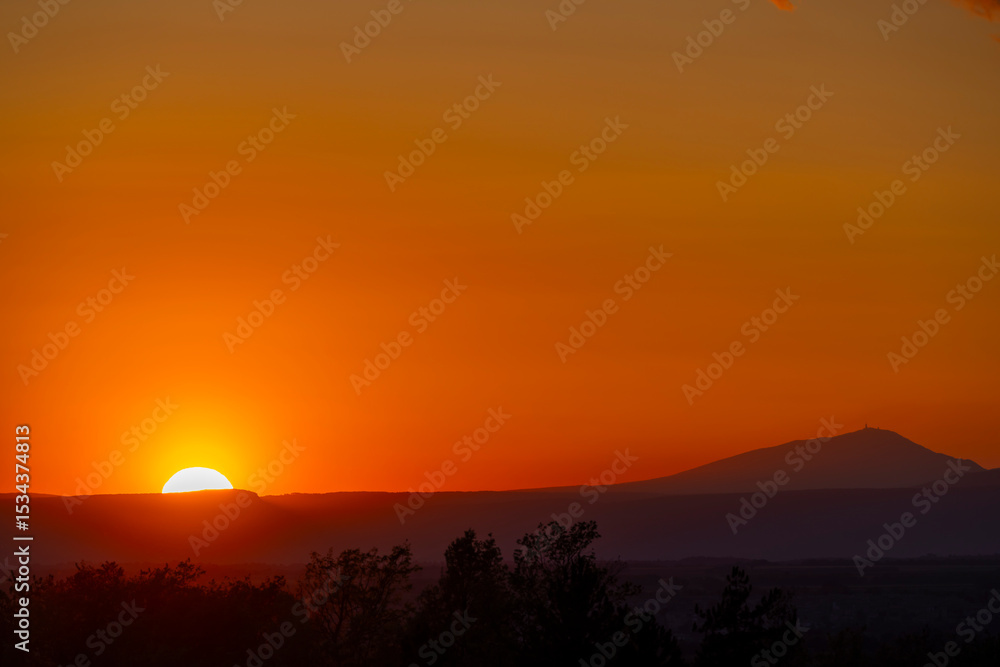 Obraz premium Bright orange sunset over mountains creating silhouettes of trees