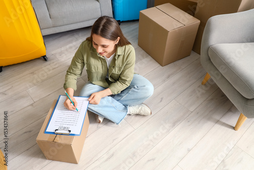 Young woman making checklist in room on moving day