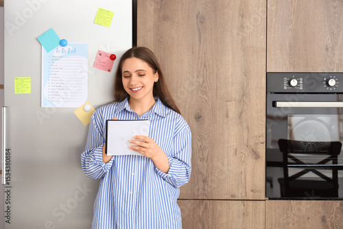 Young woman making to-do list near fridge in kitchen