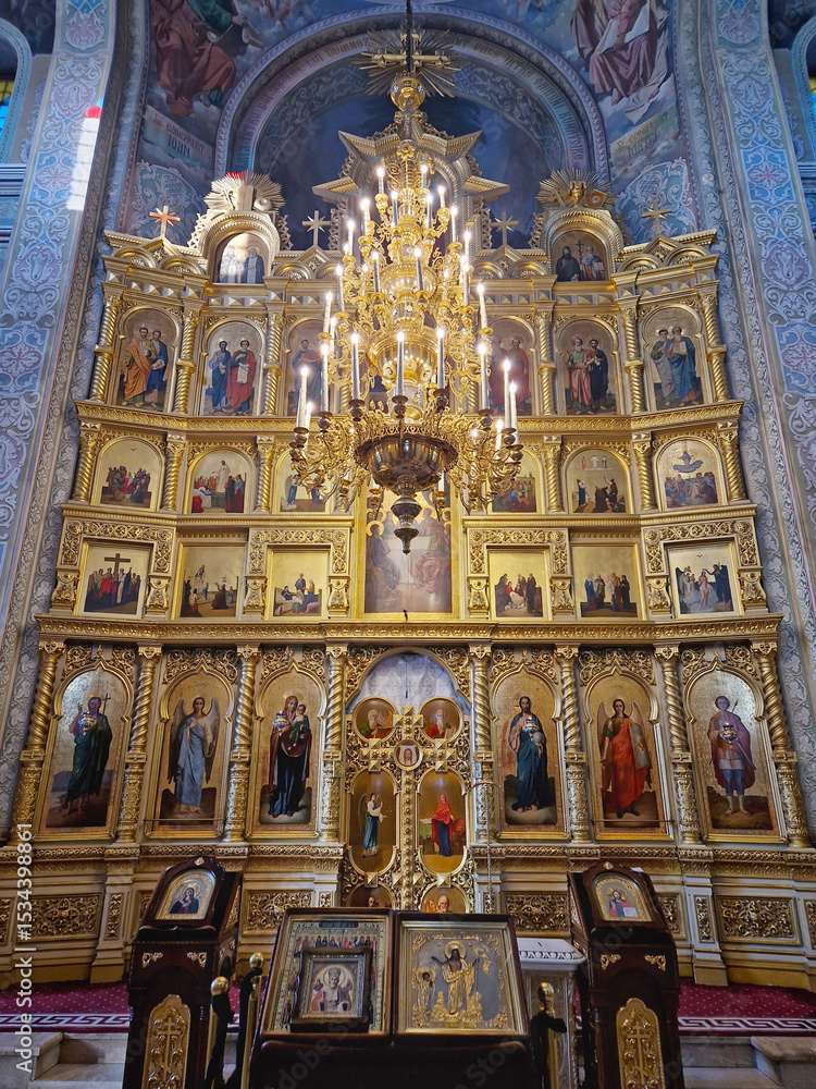 Obraz premium Capriana Monastery indoors view of traditional ornate Christian Orthodox church located in Moldova. Scene during divine service with a monk praying at the altar underneath a grand gilded chandelier