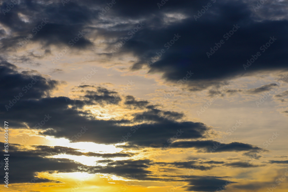 Obraz premium The evening sky, covered with dark clouds, through which golden sunbeams break through. This creates a dramatic and powerful landscape reflecting the force of nature.