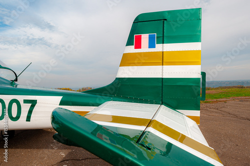 A light single-engine aircraft is preparing to take off. The tail of the aircraft is close-up, viewed from behind. The aircraft is painted green and white, with the tail number 007.