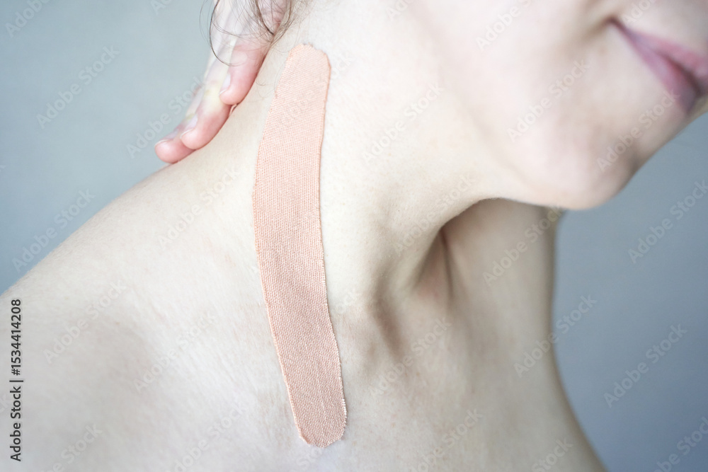 Naklejka premium Close-up of elastic beige kinesiology tape on female caucasian shoulder for muscle support and pain relief.