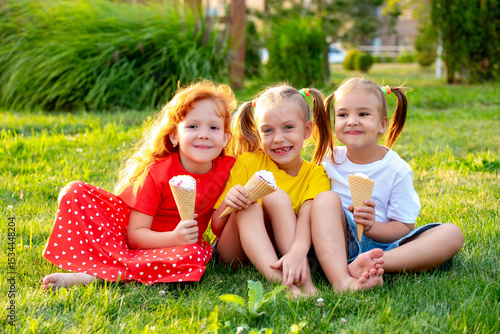 happy children eating ice cream in the summer on the green lawn in the park, a bright summer photo of children's holidays, three baby girls laughing and having fun in the summer