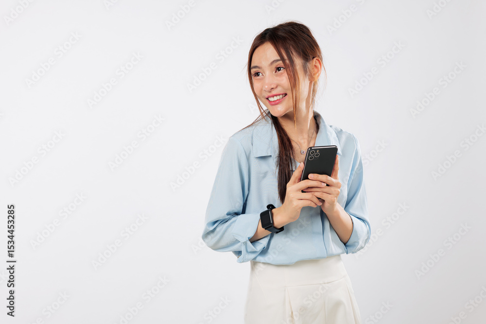 Excited Asian woman smiles, holding a mobile phone and looking to the side. She is happy with her new application on her smartphone. isolated studio white background Excited Asian woman smiles, holding a mobile phone and looking to the side. She is happy with her new application on her smartphone. isolated studio white background