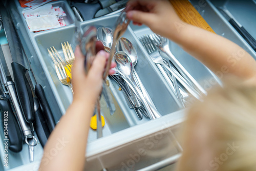 Tableau sur toile Child organizes utensils in a kitchen drawer during a sunny afternoon