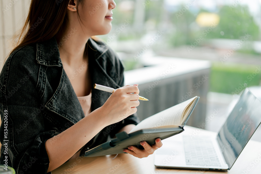 Obraz premium Beautiful Asian woman sitting working on laptop in coffee shop. Freelance translator. Young woman studying online.