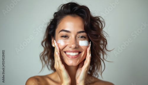 Smiling hispanic woman applying beauty cream treatment to face. Woman with curly hair, skin care products. Healthy, attractive, positive female model applying facial moisturizer, skin protection.