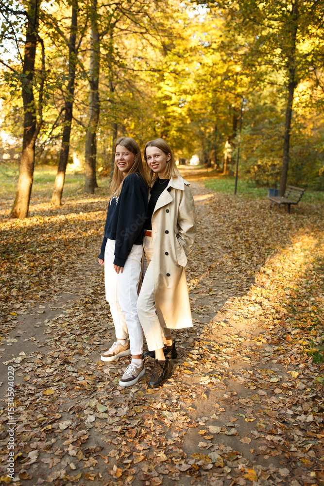Fototapeta premium Two friends pose together in a golden autumn park, enjoying the warm light and cozy atmosphere of a beautiful day.