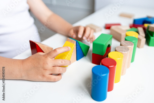 Child engaging with colorful geometric wooden blocks on white table