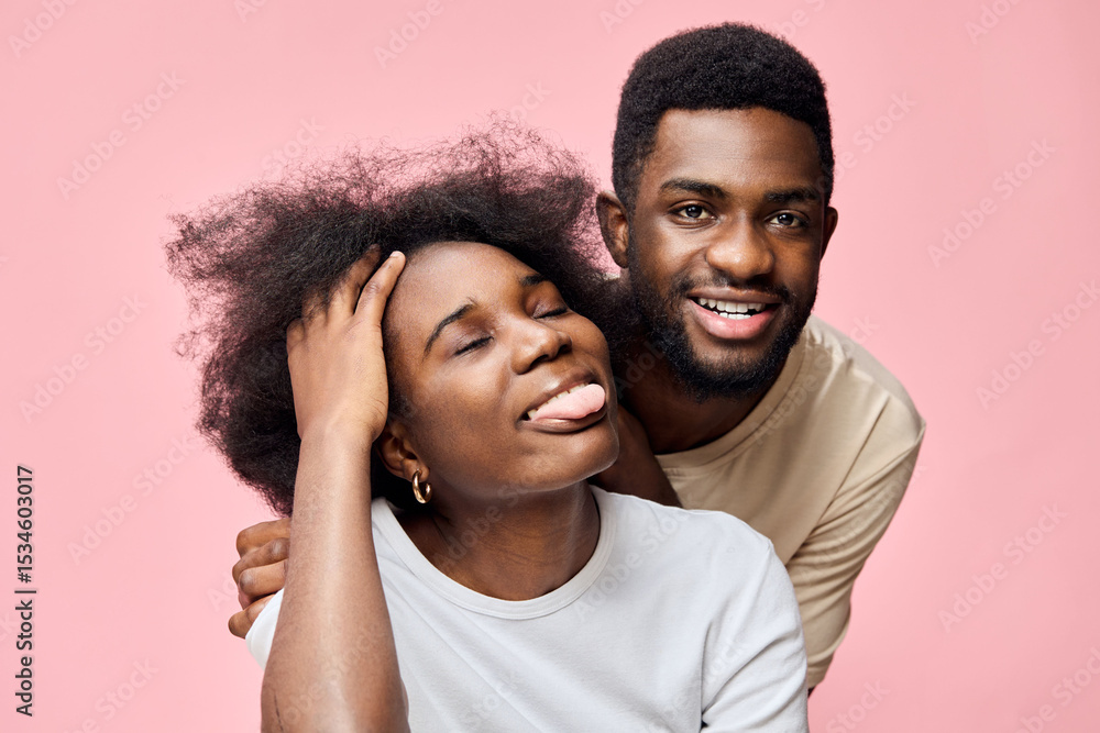 Obraz premium Happy young couple expressing joy with playful emotions on a pink background, showcasing a casual style in summer clothing and natural hairstyles