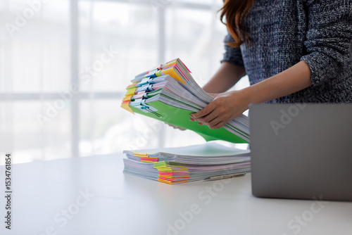 Close up of hands working in Stacks of paper files for searching and checking unfinished document achieves on folders papers on desk.
