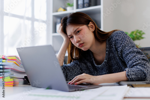 Young asian woman accountant employee Upset stressed guy suffering job problems working on laptop, headache, Bored workaholic headache and stress, migraine, stress relief, chronic pain
