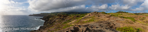 Panoramic view of a rocky coastline with green hills under a cloudy sky.