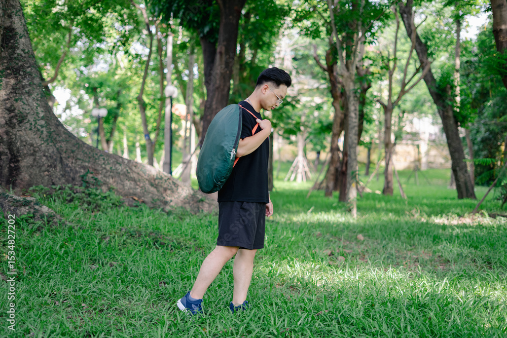 Young man walks through a lush green park carrying a large backpack during the daytime Young man walks through a lush green park carrying a large backpack during the daytime
