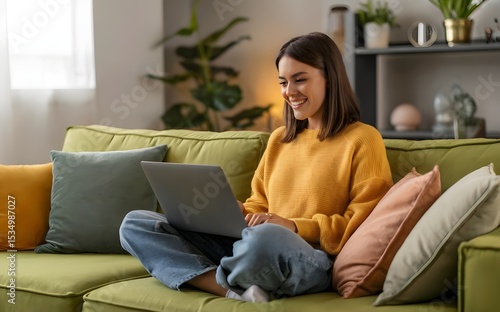 Happy young woman working on a laptop while relaxing on a cozy couch at home