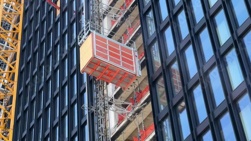 A high-rise building under construction with an yellow construction crane and an orange external Construction site elevator moving down 