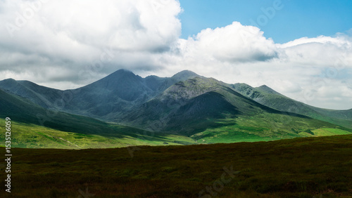 A breathtaking panorama of rolling hills and craggy mountain peaks under a pale sky. Untamed landscape.