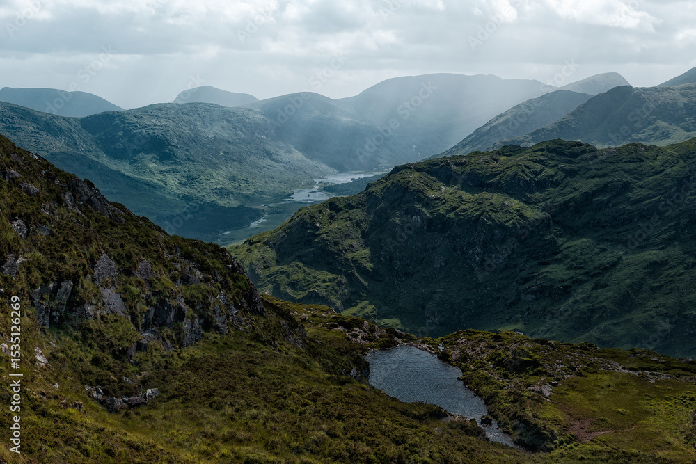 Naklejka premium A small lake sits on the hillside, overlooking the beautiful Gap of Dunloe valley. Rolling green mountains stretch into the distance in County Kerry, Ireland.