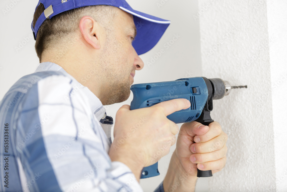 side view of young man drilling wall with electric drill side view of young man drilling wall with electric drill