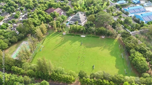 Aerial view of a green field with people a mosque and trees captured from above