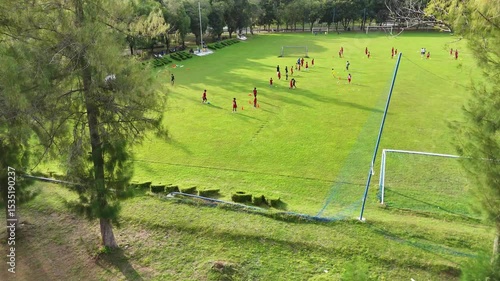 Soccer players practicing drills on a green field with goals and cones trees in the background