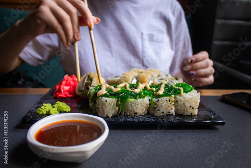 Closeup hand holding bamboo chopsticks with nigiri shrimp while soaking it in soy sauce. Detail of sushi set on wooden tray at restaurant while hand dip nigiri in soy sauce. Japanese cuisine concept.