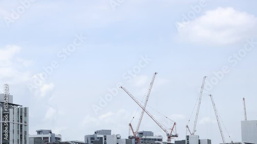 Time lapse of fluffy white clouds moving against blue sky with construction cranes in foreground. Summer nature weather sky. 