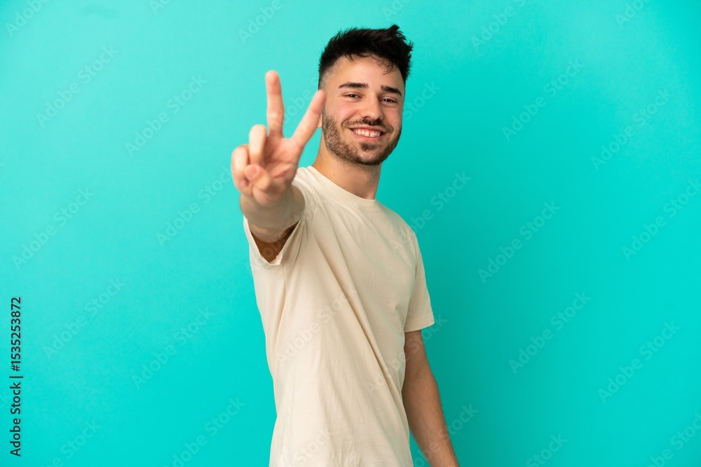 Fototapeta premium Young caucasian man isolated on blue background smiling and showing victory sign