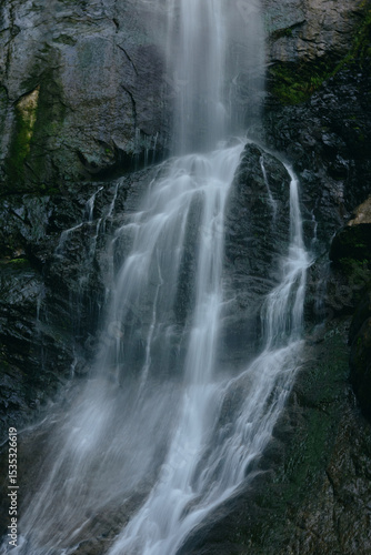 flowing waterfall cascading over dark mossy rocks in a serene forest setting with soft natural light and cool tones