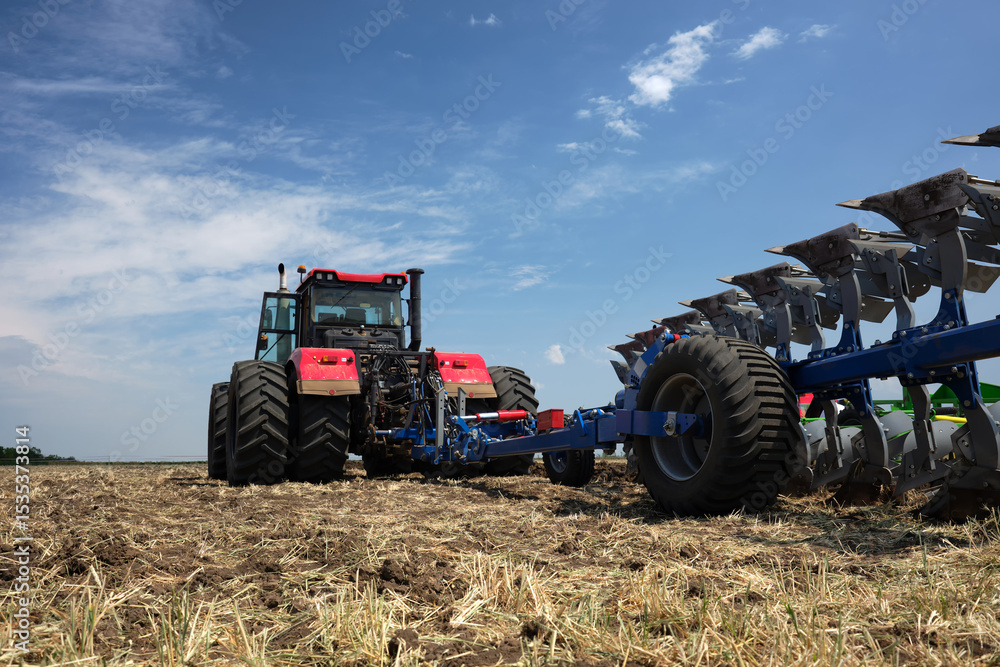 Fototapeta premium Rear view of a large tractor work with a plow in a field. Start tillage after harvest.