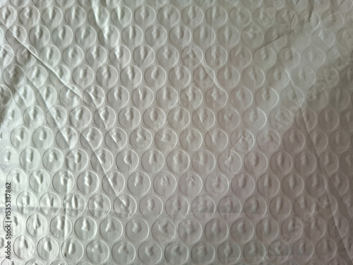 Bubble wrap texture with circular patterns of translucent plastic, featuring wrinkles and creases. The surface catches light, creating subtle reflections and shadows on each bubble