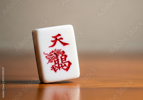 Close-up of Chinese mahjong tile with red dragon symbol on wooden surface. International Mahjong Day