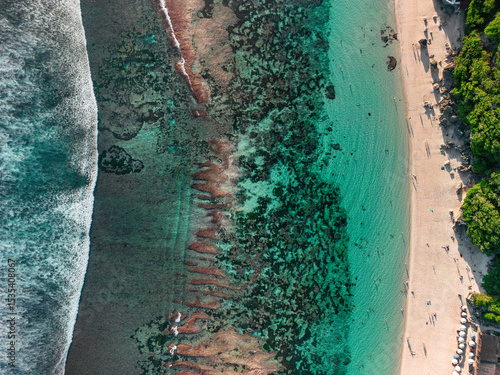 Bright turquoise waters lap the sandy shores of Melasti Beach in the summer sun in Bali.