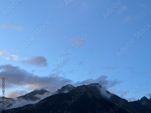 Mountain peaks with low clouds under clear blue sky