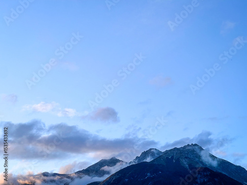 Mountain peaks with low clouds under clear blue sky
