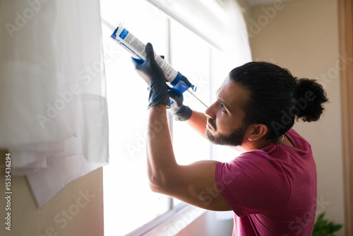 Fotografía Man applying silicone sealant to window frame at home
