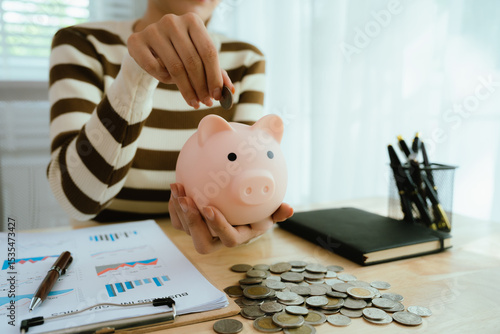 An Asian woman is putting money in a piggy bank while looking at a calculator, giving advice on financial planning.