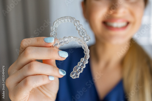 Smiling woman holding transparent dental aligner braces for orthodontic treatment