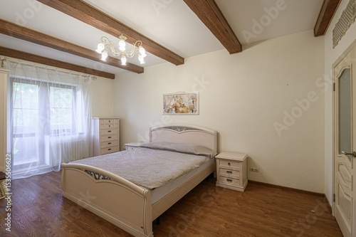 Bedroom with a light-colored bed, wooden beams, and natural light